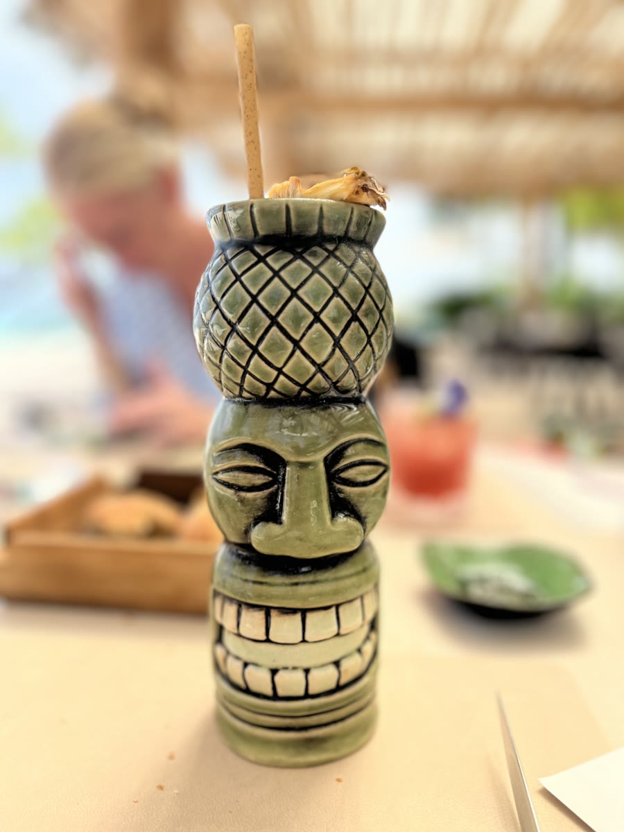A green tiki mug topped with pineapple, served on a beachside table
